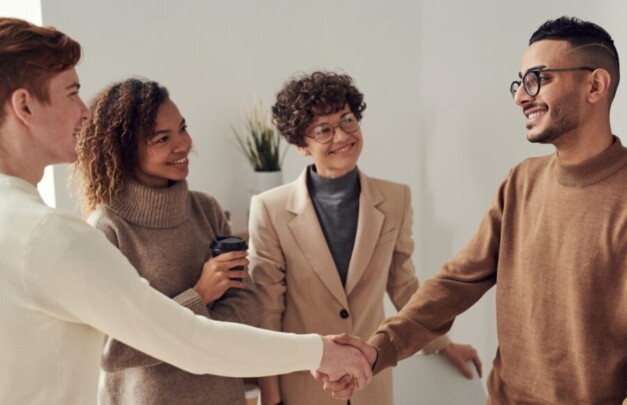 Diverse group of young adults shaking hands in an office environment, depicting teamwork and collaboration